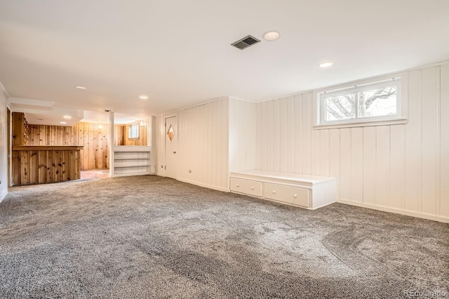 below grade area with carpet flooring, wood walls, and visible vents