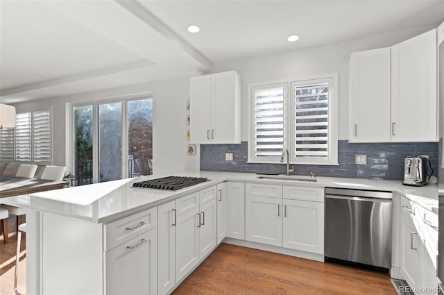 kitchen with light wood-style flooring, a peninsula, stainless steel appliances, a healthy amount of sunlight, and a sink