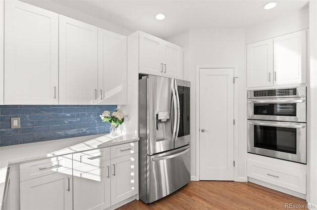 kitchen featuring stainless steel appliances, white cabinets, light countertops, light wood finished floors, and tasteful backsplash