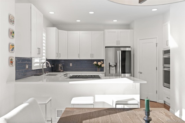 kitchen with tasteful backsplash, appliances with stainless steel finishes, a peninsula, white cabinetry, and a sink