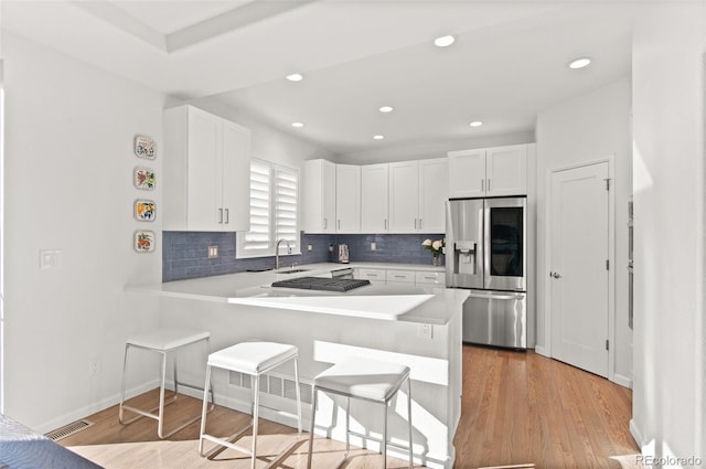 kitchen with a sink, visible vents, a kitchen breakfast bar, light countertops, and stainless steel fridge