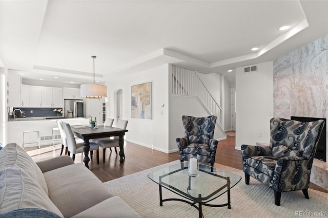 living room featuring a raised ceiling, stairway, and light wood finished floors