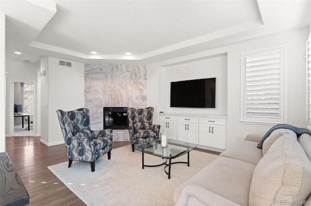 living area with recessed lighting, wood finished floors, visible vents, baseboards, and a tray ceiling