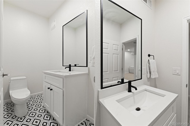 bathroom featuring two vanities, a sink, toilet, and baseboards