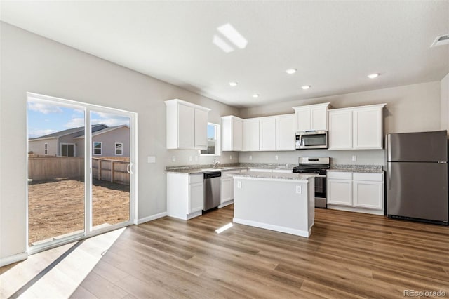 979 Cascade Falls St, Severance, CO 80550 - kitchen with appliances with stainless steel finishes, wood finished floors, recessed lighting, white cabinetry, and a center island