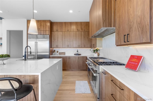 13415 S Resort Dr, Conifer, CO 80433 - kitchen with high end appliances, wall chimney exhaust hood, light stone countertops, brown cabinetry, and recessed lighting