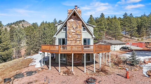 rear view of property with a chimney, stone siding, a fire pit, and a wooden deck