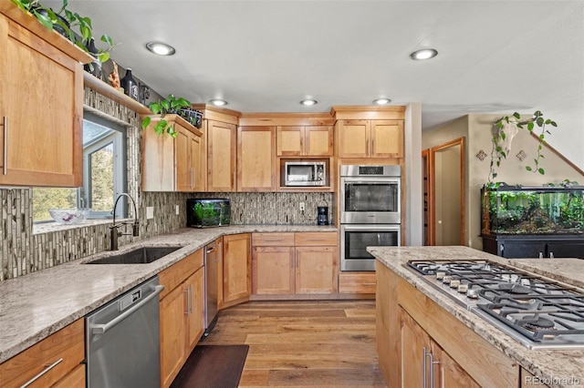 kitchen featuring light brown cabinets, decorative backsplash, light wood-style flooring, stainless steel appliances, and a sink