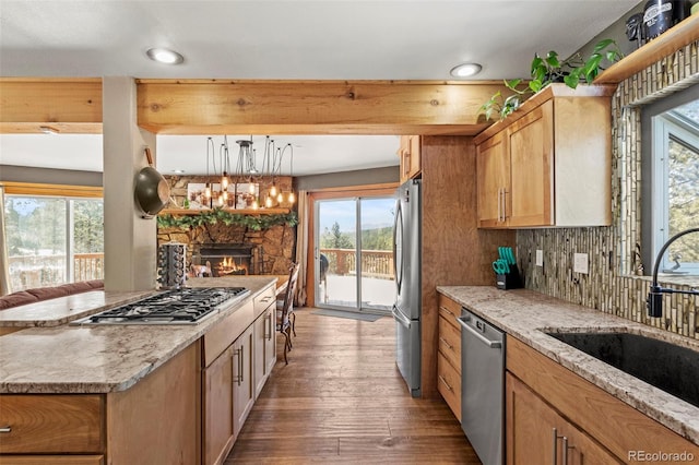 kitchen featuring a sink, wood finished floors, stainless steel appliances, a stone fireplace, and light stone countertops