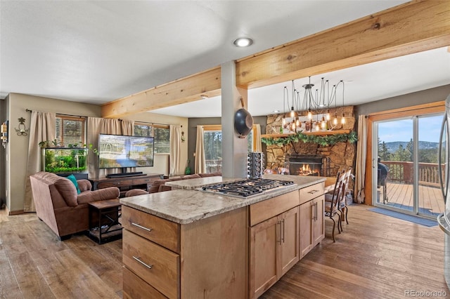 kitchen with pendant lighting, open floor plan, wood-type flooring, stainless steel gas stovetop, and a fireplace