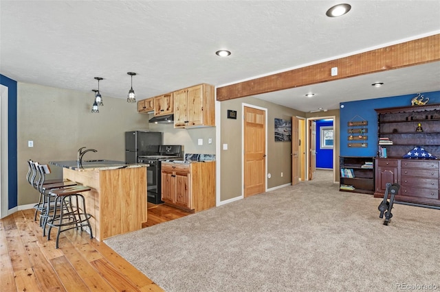 kitchen featuring under cabinet range hood, gas stove, a breakfast bar area, and baseboards