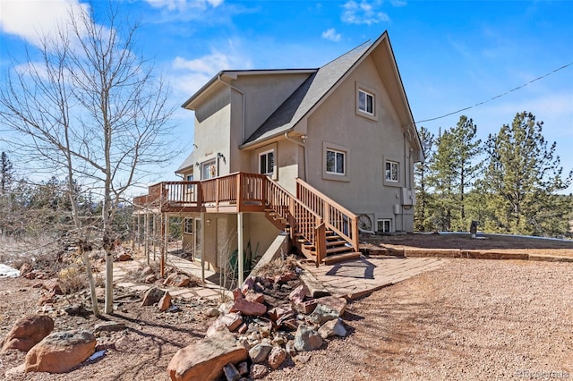 rear view of property featuring stairs, a deck, and stucco siding