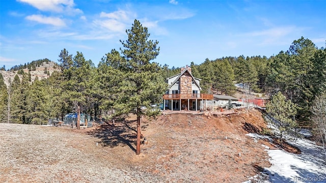 back of property with a view of trees, stone siding, and a chimney