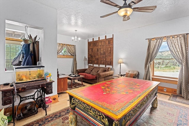 interior space featuring ceiling fan with notable chandelier, light hardwood / wood-style flooring, and a textured ceiling