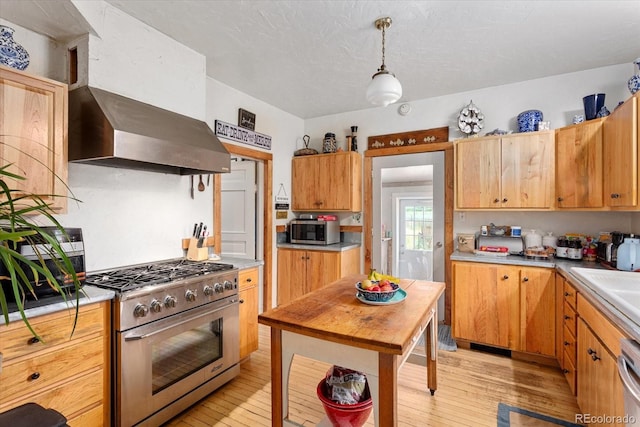 kitchen featuring pendant lighting, appliances with stainless steel finishes, light hardwood / wood-style floors, a textured ceiling, and wall chimney exhaust hood