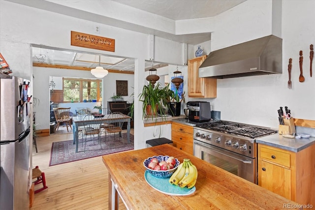 kitchen with stainless steel appliances, pendant lighting, wall chimney range hood, and light wood-type flooring