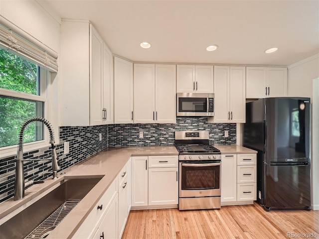 kitchen featuring light wood-type flooring, tasteful backsplash, sink, white cabinets, and appliances with stainless steel finishes