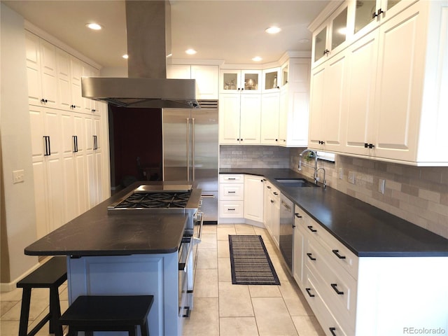 kitchen with island range hood, a sink, dark countertops, premium appliances, and light tile patterned flooring
