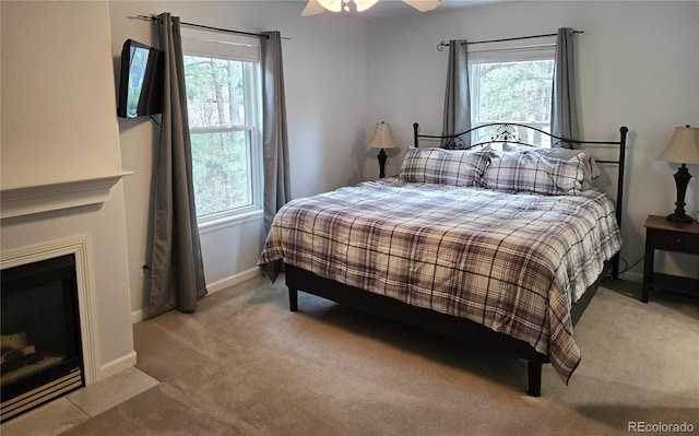 carpeted bedroom with multiple windows, a fireplace with flush hearth, baseboards, and a ceiling fan