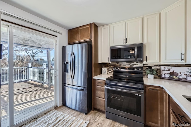 kitchen featuring light countertops, light wood-style flooring, decorative backsplash, appliances with stainless steel finishes, and white cabinets