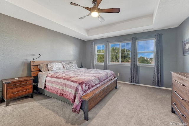 bedroom featuring ceiling fan, light colored carpet, and a tray ceiling