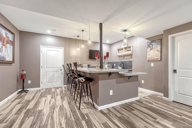 kitchen with kitchen peninsula, hardwood / wood-style floors, pendant lighting, and a breakfast bar