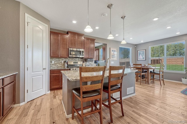 kitchen featuring decorative light fixtures, a kitchen island with sink, stainless steel appliances, and light hardwood / wood-style flooring