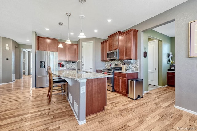 kitchen featuring light hardwood / wood-style flooring, decorative light fixtures, appliances with stainless steel finishes, and a kitchen island with sink