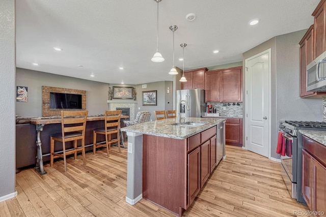 kitchen featuring appliances with stainless steel finishes, pendant lighting, light hardwood / wood-style flooring, and an island with sink