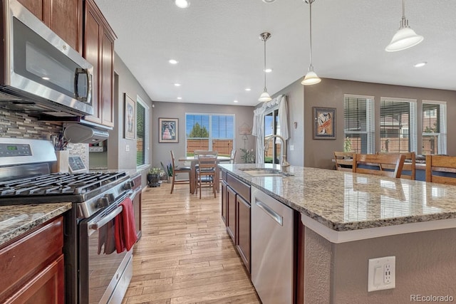 kitchen featuring a center island with sink, appliances with stainless steel finishes, plenty of natural light, and light hardwood / wood-style flooring