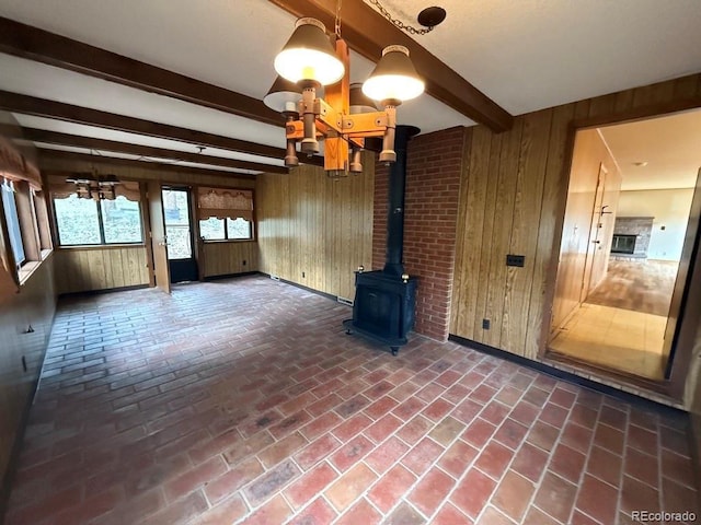 1013 Lexington Ln, Estes Park, CO 80517 - unfurnished living room featuring wooden walls, a chandelier, beam ceiling, a wood stove, and brick floors