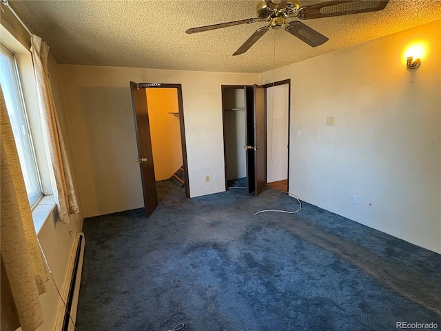 unfurnished bedroom with a textured ceiling, baseboard heating, multiple closets, dark carpet, and ceiling fan