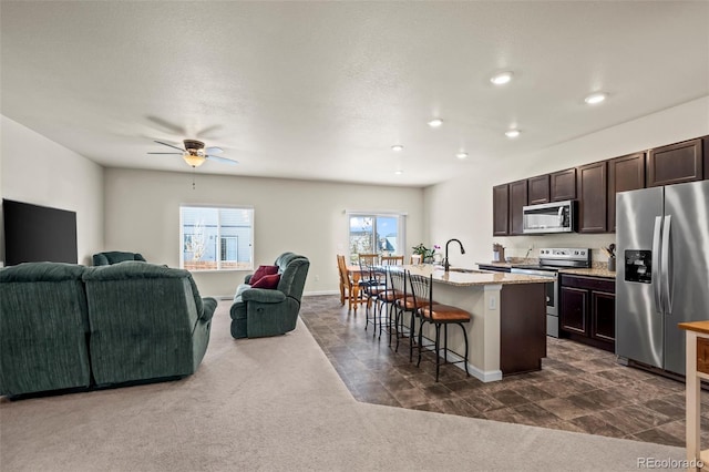 1868 Homestead Dr, Fort Lupton, CO 80621 - kitchen featuring appliances with stainless steel finishes, dark colored carpet, open floor plan, a breakfast bar area, and dark brown cabinets