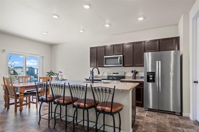 1868 Homestead Dr, Fort Lupton, CO 80621 - kitchen with stainless steel appliances, a kitchen breakfast bar, dark brown cabinets, a kitchen island with sink, and recessed lighting