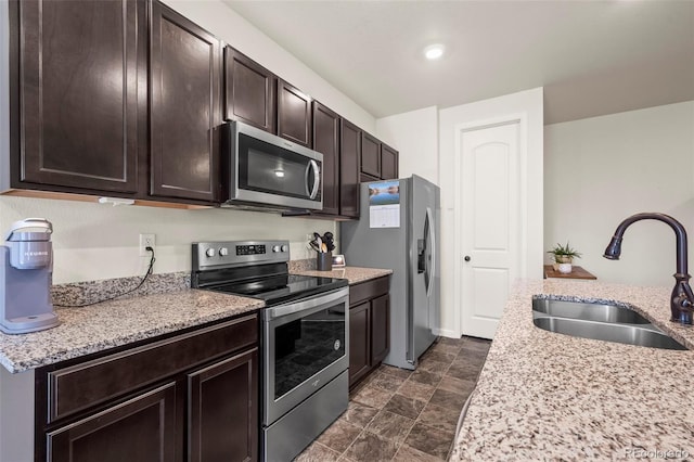 1868 Homestead Dr, Fort Lupton, CO 80621 - kitchen with appliances with stainless steel finishes, a sink, dark brown cabinets, light stone counters, and stone finish flooring