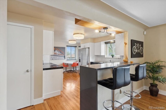 kitchen featuring stainless steel fridge with ice dispenser, light wood-type flooring, a peninsula, white cabinetry, and dark countertops