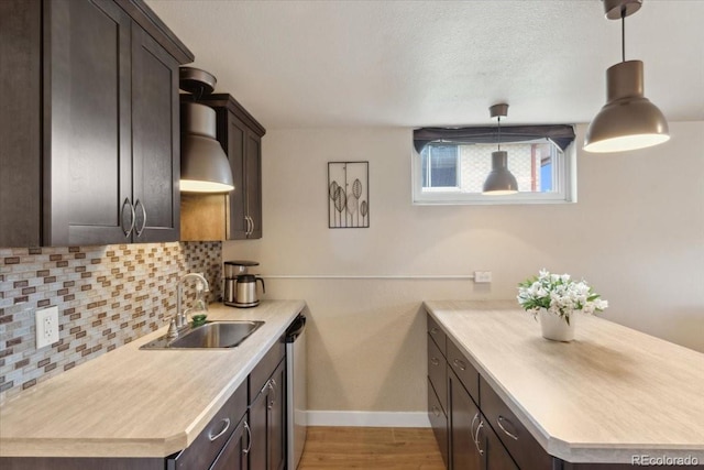 kitchen with dark brown cabinetry, light countertops, a sink, baseboards, and backsplash