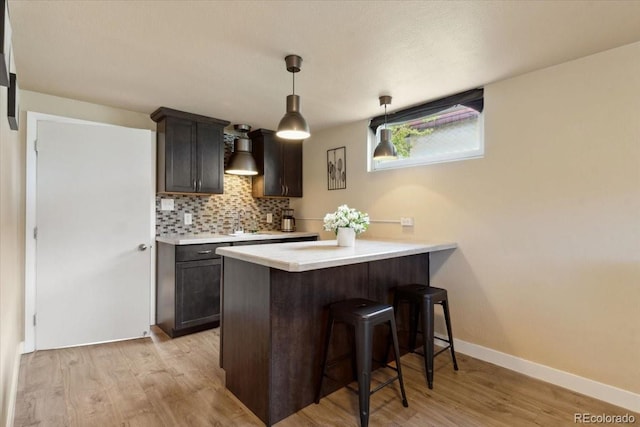 kitchen with tasteful backsplash, light countertops, light wood-type flooring, a peninsula, and a kitchen bar