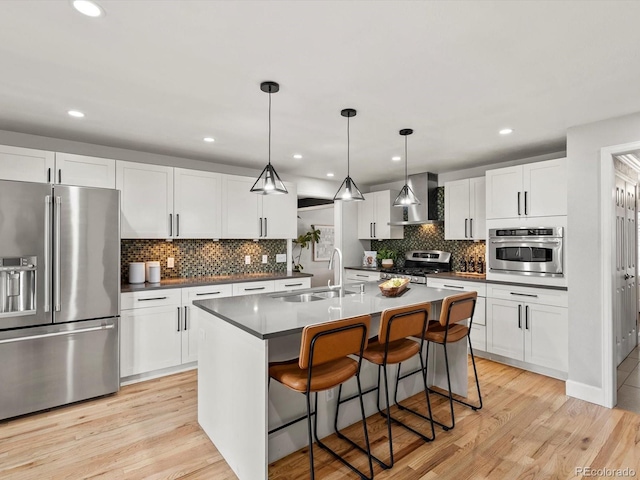 7055 E Heritage Pl S, Centennial, CO 80111 - kitchen featuring stainless steel appliances, a sink, wall chimney range hood, tasteful backsplash, and light wood-style floors