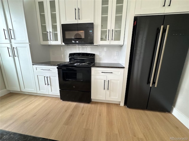 kitchen featuring glass insert cabinets, dark countertops, light wood-style flooring, and black appliances