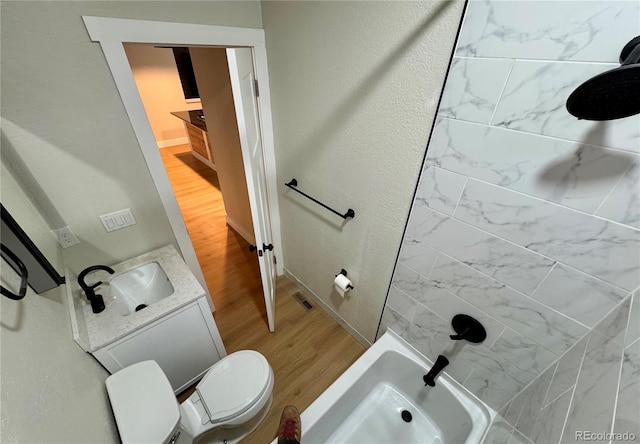 bathroom with a textured wall, toilet, wood finished floors, vanity, and walk in shower