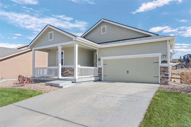 view of front of home featuring driveway, covered porch, a garage, and stone siding