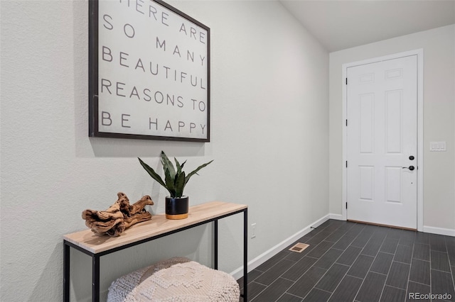 foyer featuring baseboards, vaulted ceiling, and dark wood-type flooring