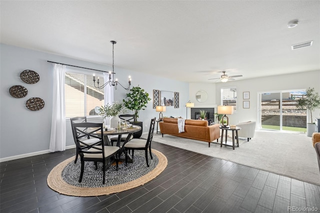 dining area with a fireplace, baseboards, dark wood finished floors, and ceiling fan with notable chandelier