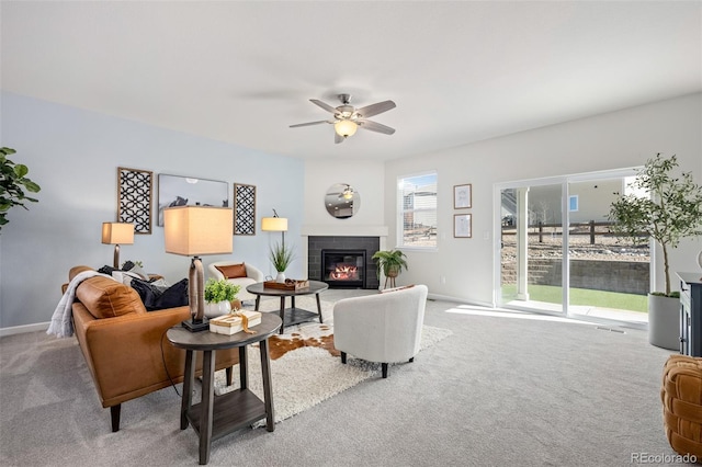 carpeted living area featuring ceiling fan, baseboards, and a tiled fireplace