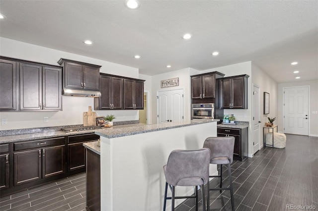 kitchen with appliances with stainless steel finishes, dark brown cabinetry, under cabinet range hood, and a kitchen breakfast bar