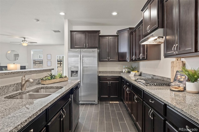 kitchen with under cabinet range hood, appliances with stainless steel finishes, light stone counters, and a sink