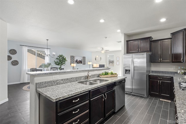 kitchen with a center island with sink, light stone countertops, stainless steel appliances, a sink, and recessed lighting