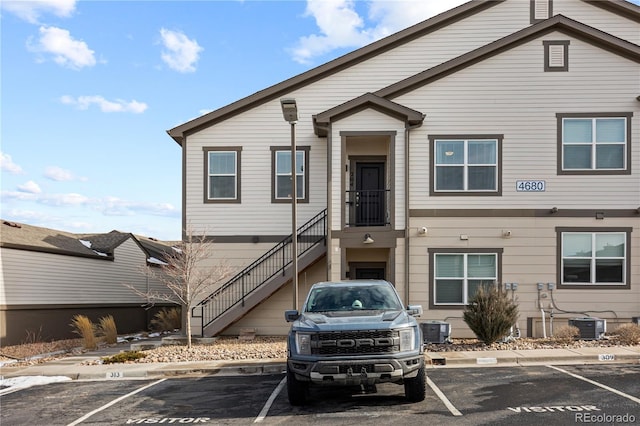 multi unit property with central AC unit, stairway, and uncovered parking