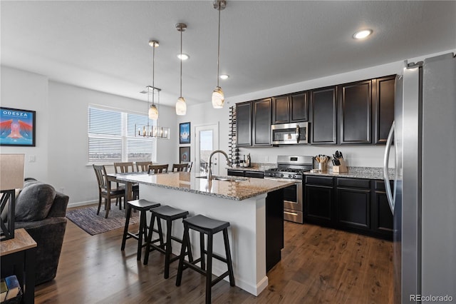 kitchen with dark wood-style flooring, light stone countertops, a kitchen bar, stainless steel appliances, and a sink